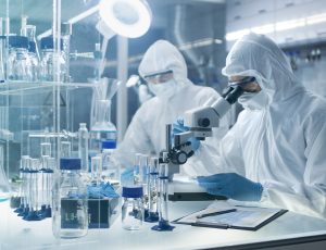 In a Secure High Level Laboratory Scientists in a Coverall Conducting a Research. Chemist Adjusts Samples in a  Petri Dish with Pincers and then Examines Them Under Microscope.