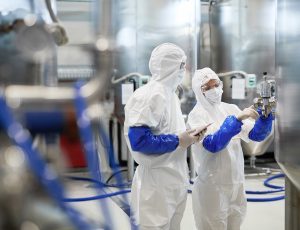 Side view portrait of two workers wearing protective suits while using equipment at modern chemical plant, copy space